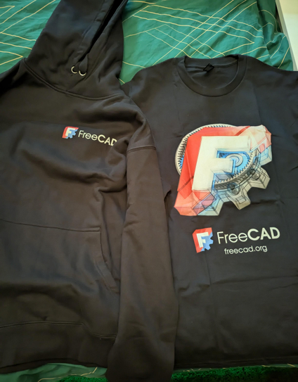 A black hoody and a black shirt. The hoody has a FreeCAD logo and small text. The shirt has a bigger logo with text and a big FreeCAD graphic.